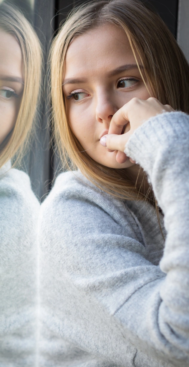 woman with hand at her mouth looking out window